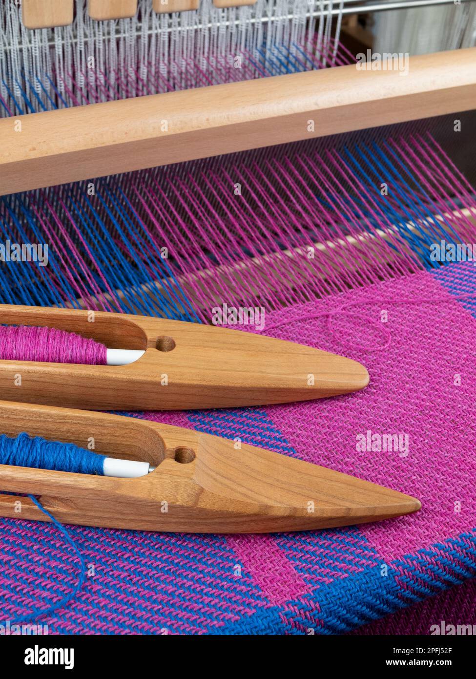 Hölzerne Shuttles mit blauen und rosafarbenen Fäden auf dem Tischkabelbaum, vertikales Format. Handwebwebstoffüberwachung, Textilherstellung Stockfoto