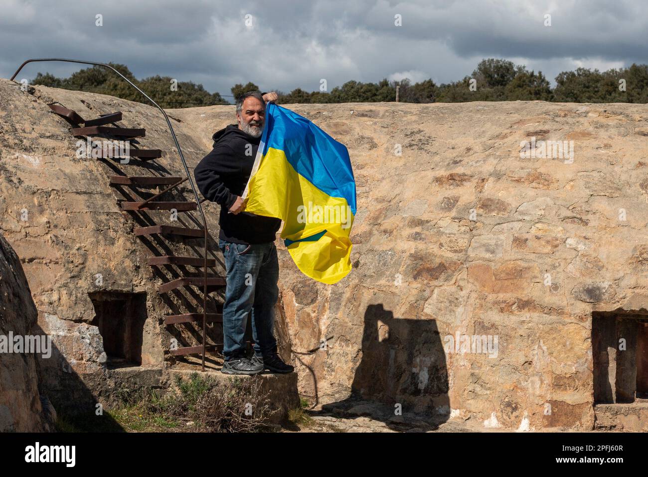 Ein erwachsener Mann, der eine ukrainische Flagge in einem militärischen Verteidigungsbau, einem Bunker, hält. Stockfoto