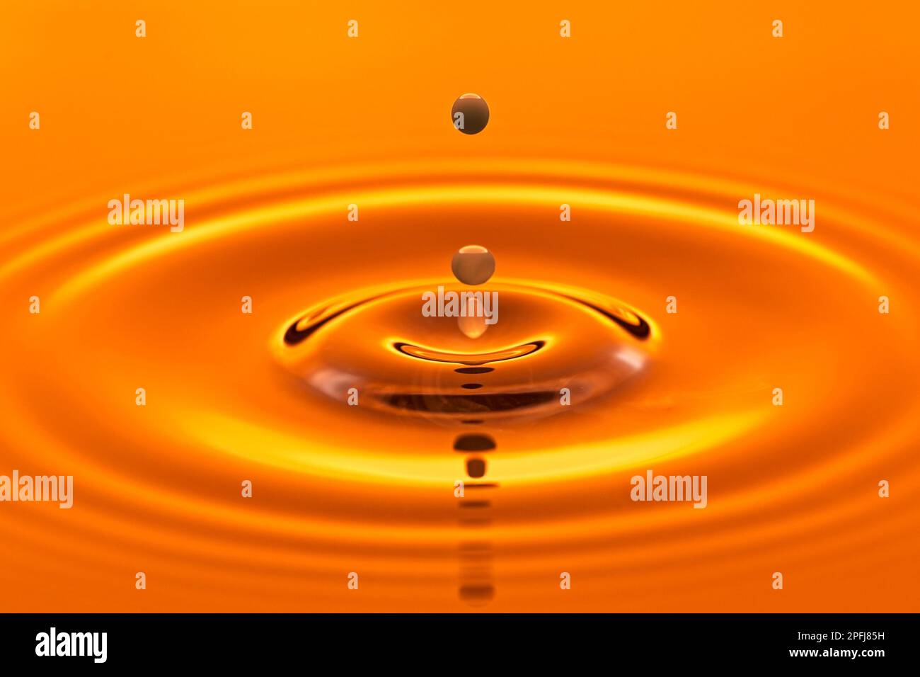 Ein abstraktes Studiofoto eines Wassertropfens, der in stilles Wasser mit Hintergrundbeleuchtung eines orangefarbenen Studiostroboskopes spritzt. Stockfoto