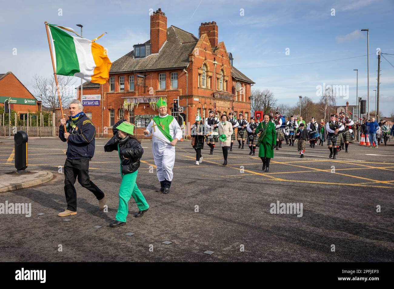 2023 St. Patrick's Day Parade in Orford Lane Warrington. Die irische Flagge führt die Prozession an, wenn sie die Straße überqueren Stockfoto