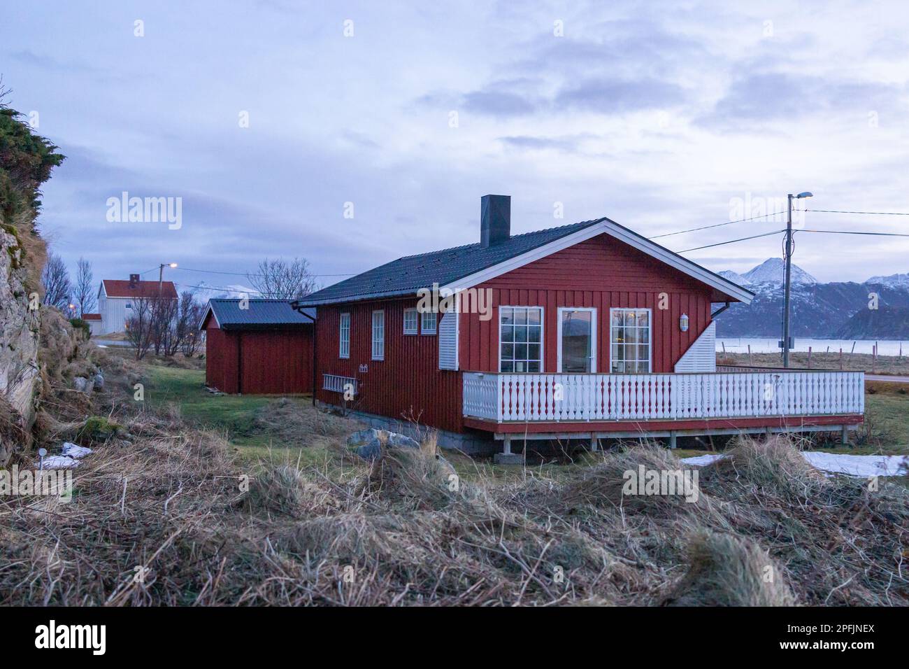 Farbenfrohe Häuser am Ufer des Nordatlantiks mit Windmühle. Hölzerne Ferienhäuser auf den Inseln Hillesøy und Sommarøy. Rotes Haus am See Stockfoto