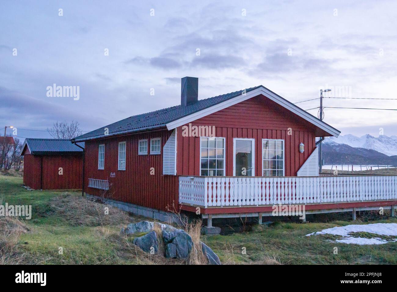 Farbenfrohe Häuser am Ufer des Nordatlantiks mit Windmühle. Hölzerne Ferienhäuser auf den Inseln Hillesøy und Sommarøy. Rotes Haus am See Stockfoto