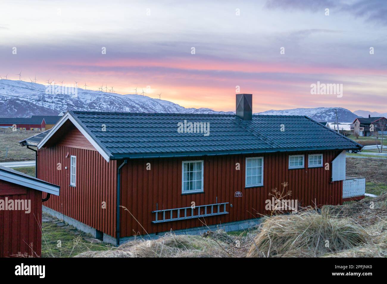 Farbenfrohe Häuser am Ufer des Nordatlantiks mit Windmühle. Hölzerne Ferienhäuser auf den Inseln Hillesøy und Sommarøy. Rotes Haus am See Stockfoto