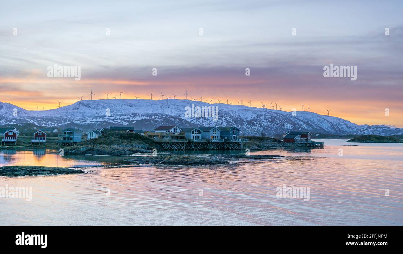 Farbenfrohe Häuser am Ufer des Nordatlantiks mit Windmühle. Hölzerne Ferienhäuser auf den Inseln Hillesøy und Sommarøy. Rotes Haus am See Stockfoto