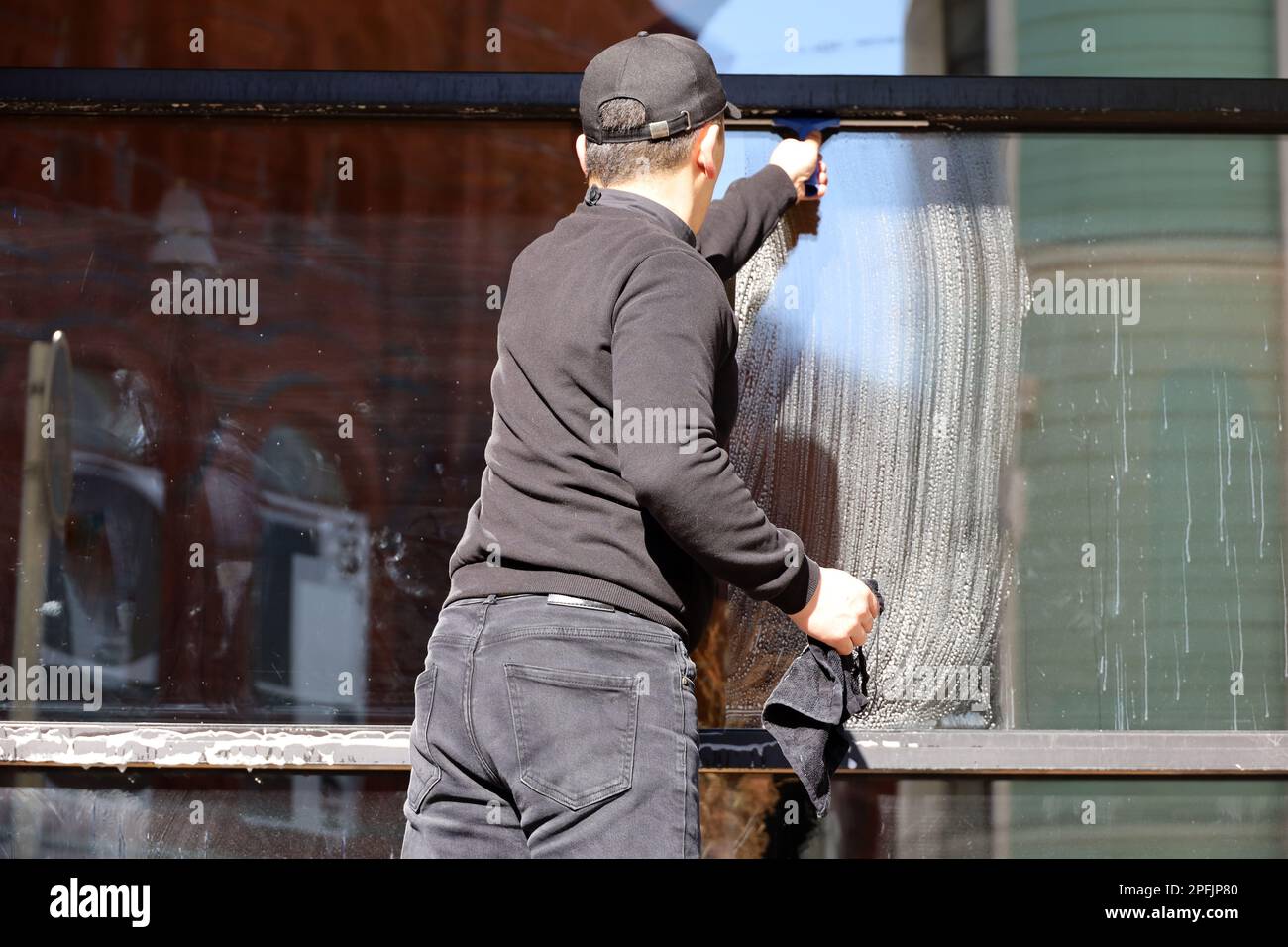 Fensterputzer, männlicher Arbeiter wäscht das Glas der Straßencafe Fassade. Reinigung in der Frühlingsstadt Stockfoto