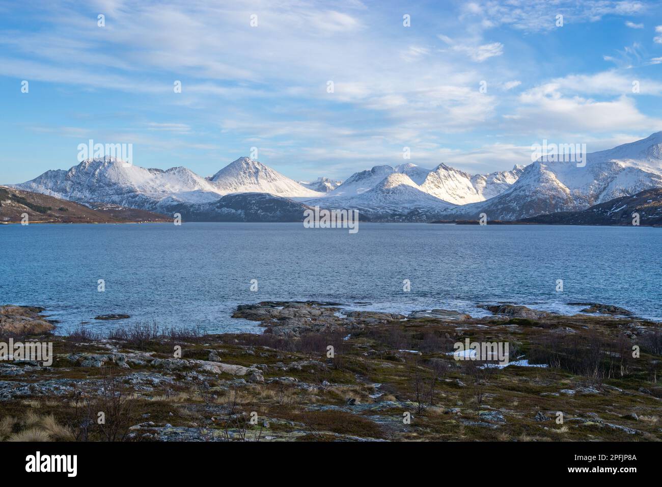 Stürmischer Ozean am Ufer von Hillesøya, in Troms, Norwegen, mit Wellen an der Küste kleiner Inseln, mit schneebedeckten Bergen im Hintergrund. Stockfoto