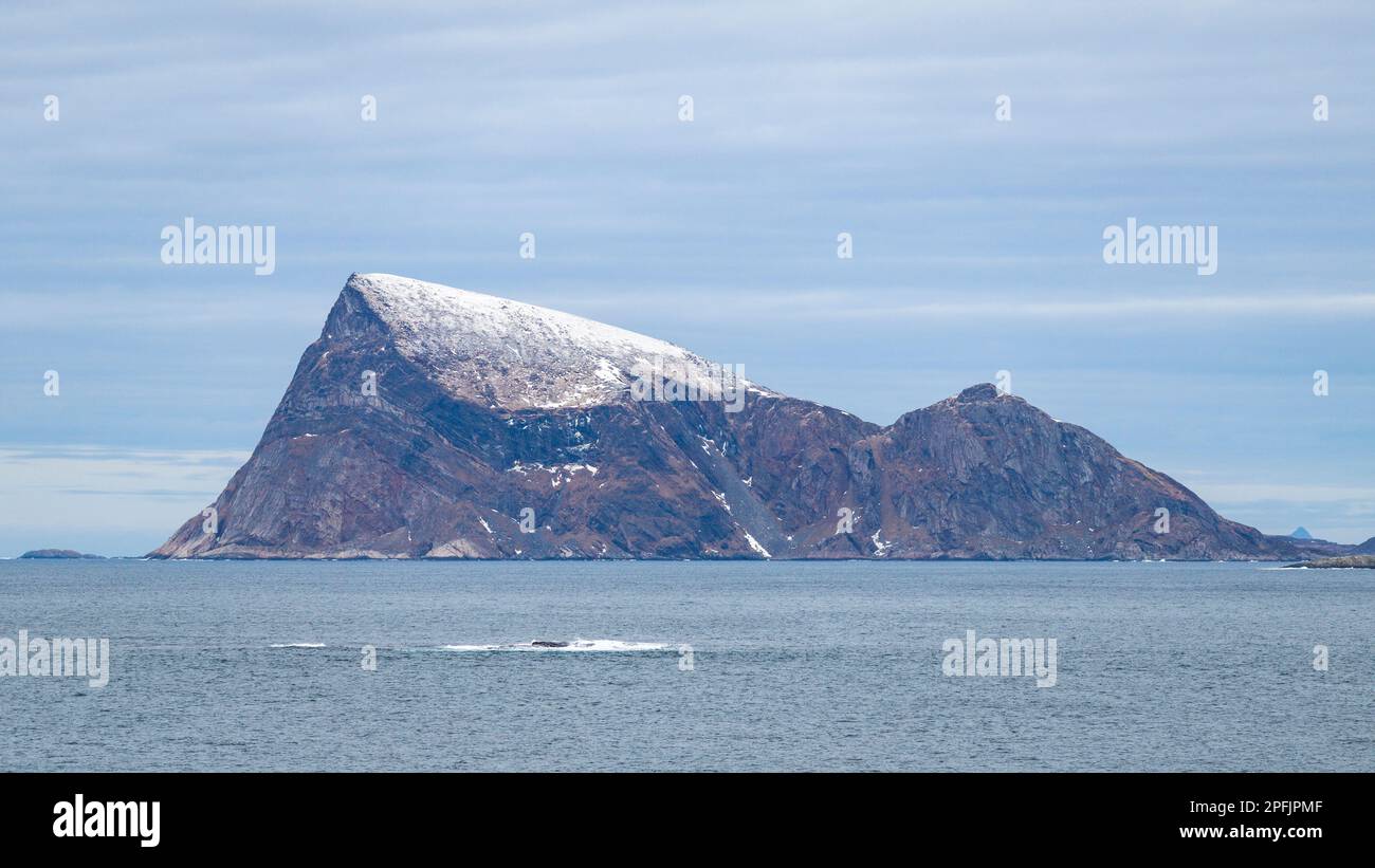 Stürmischer Ozean am Ufer von Hillesøya, in Troms, Norwegen, mit Wellen an der Küste kleiner Inseln, mit schneebedeckten Bergen im Hintergrund. Stockfoto