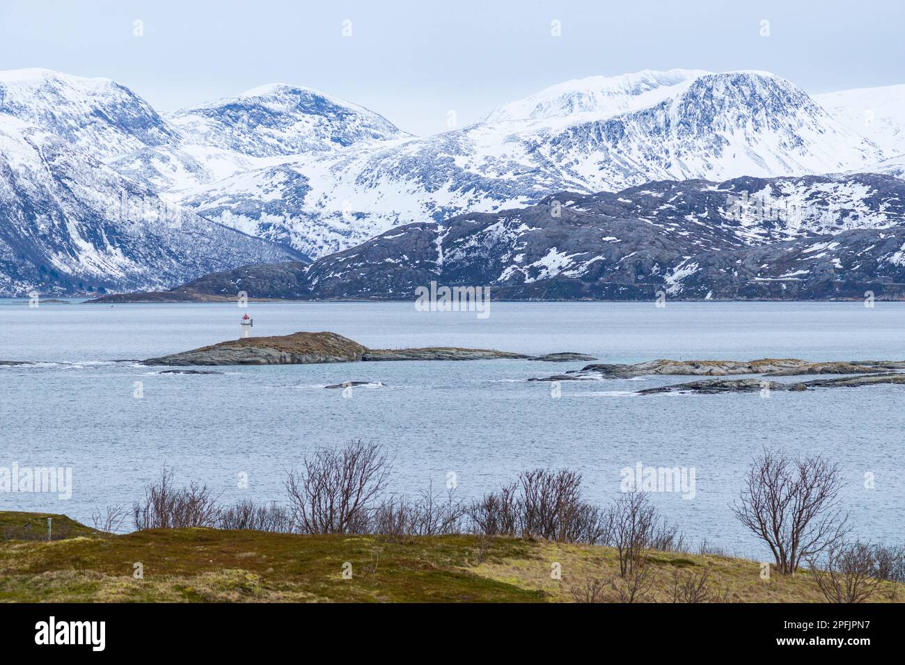 Stürmischer Ozean am Ufer von Hillesøya, in Troms, Norwegen, mit Wellen an der Küste kleiner Inseln, mit schneebedeckten Bergen im Hintergrund. Stockfoto
