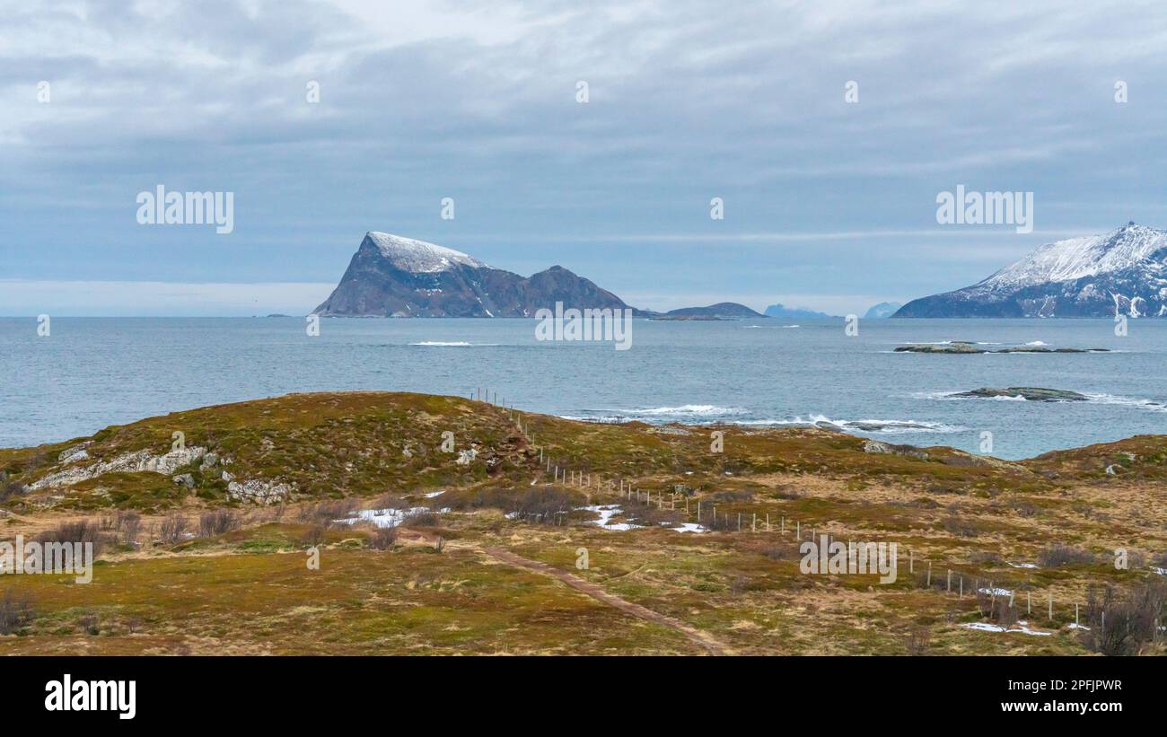 Stürmischer Ozean am Ufer von Hillesøya, in Troms, Norwegen, mit Wellen an der Küste kleiner Inseln, mit schneebedeckten Bergen im Hintergrund. Stockfoto
