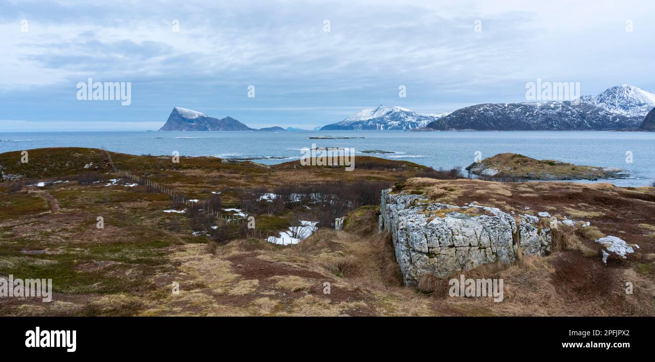 Stürmischer Ozean am Ufer von Hillesøya, in Troms, Norwegen, mit Wellen an der Küste kleiner Inseln, mit schneebedeckten Bergen im Hintergrund. Stockfoto