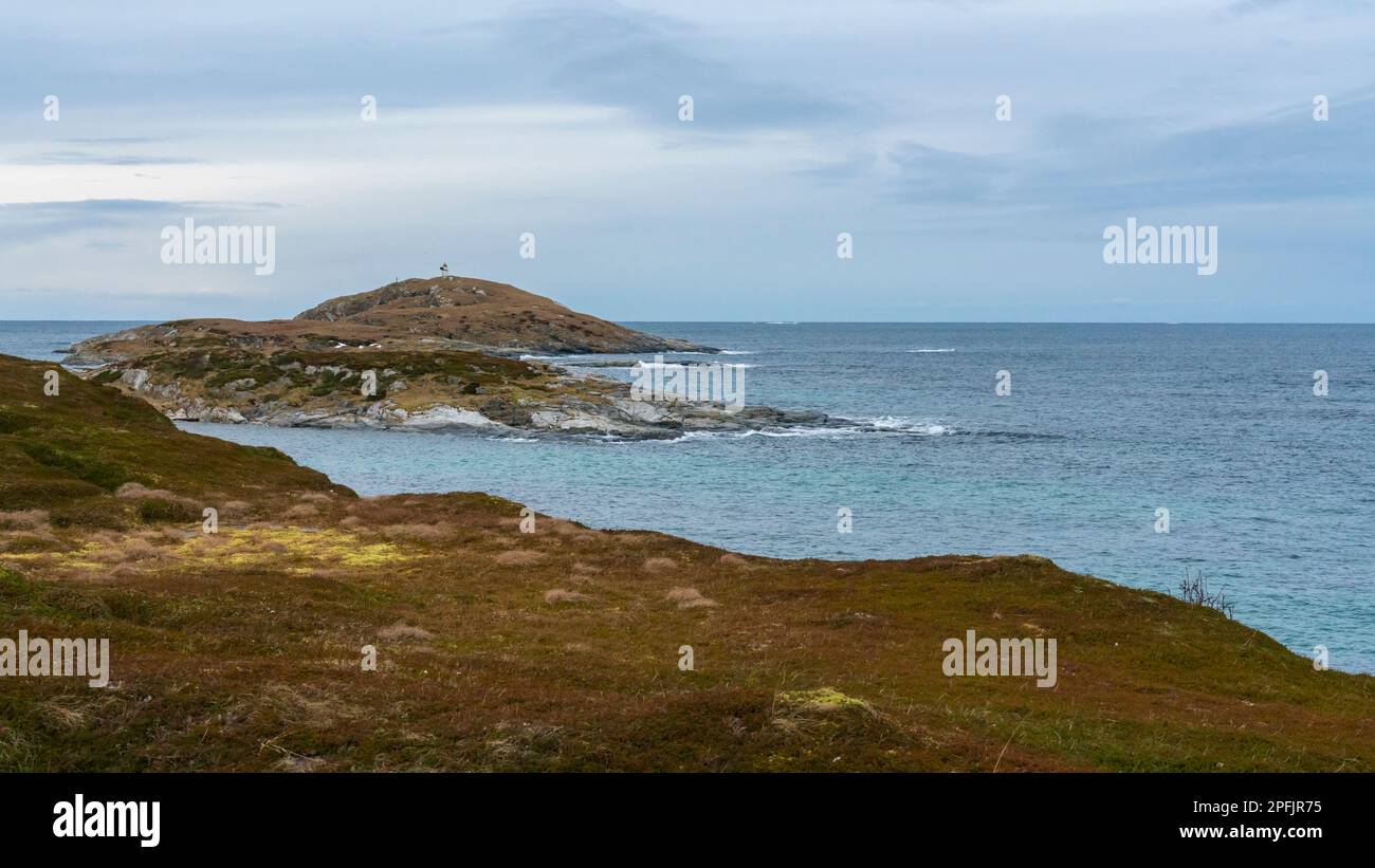 Stürmischer Ozean am Ufer von Hillesøya, in Troms, Norwegen, mit Wellen an der Küste kleiner Inseln, mit schneebedeckten Bergen im Hintergrund. Stockfoto