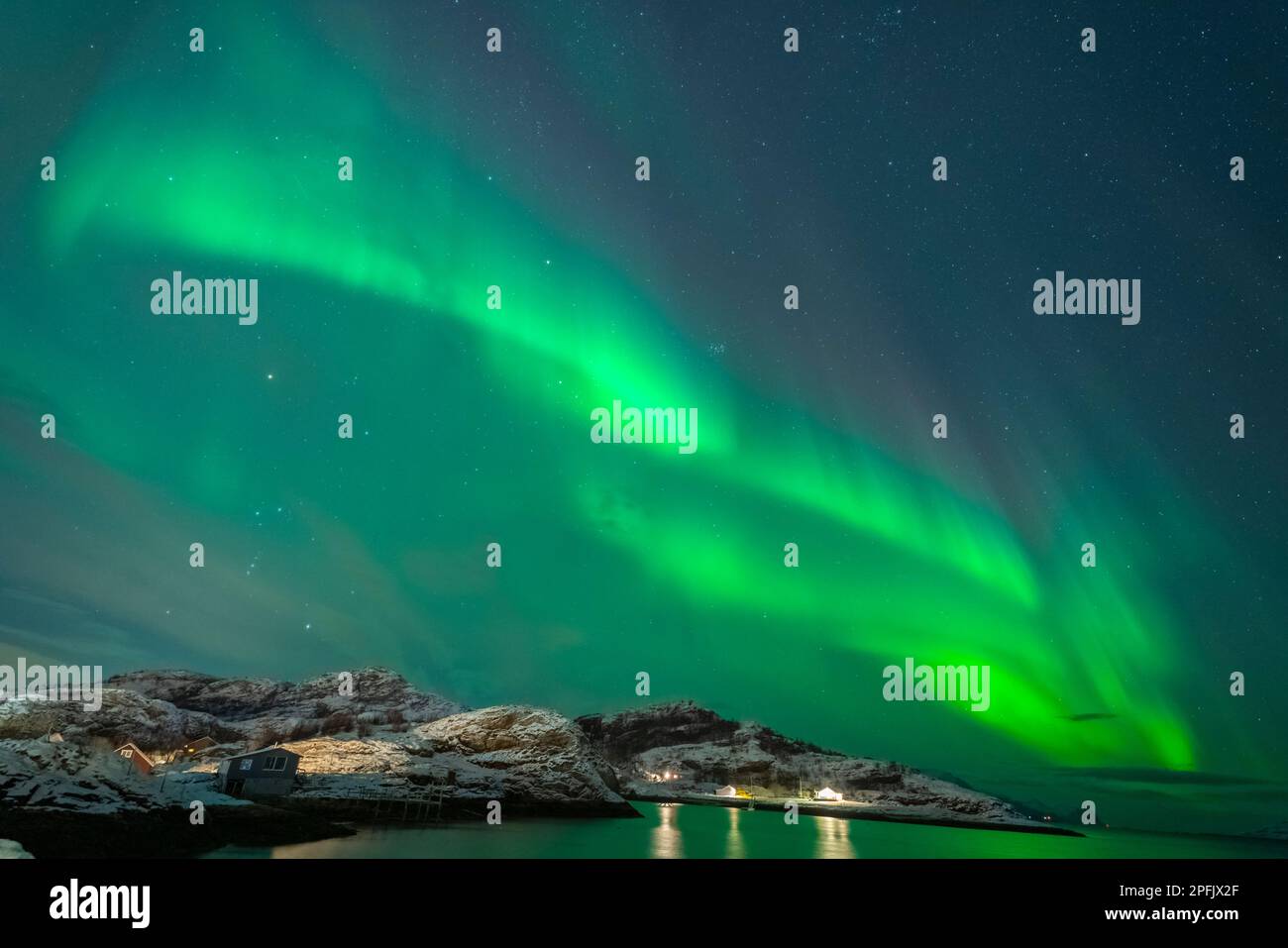 tanzende Nordlichter über dem Dorf Brensholmen auf der Insel Kvaløya. Farbige Aurora Borealis spiegeln sich im Meer. Polarlicht in Troms, Norwegen Stockfoto