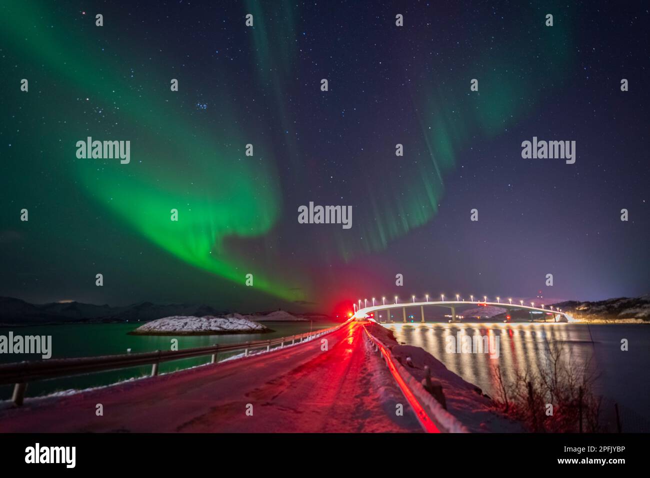 Schöne Nordlichter über der beleuchteten Brücke von Sommarøy mit der roten Ampel. tanzende Polarlichter, die sich im Wasser des Nordatlantiks Spiels Stockfoto