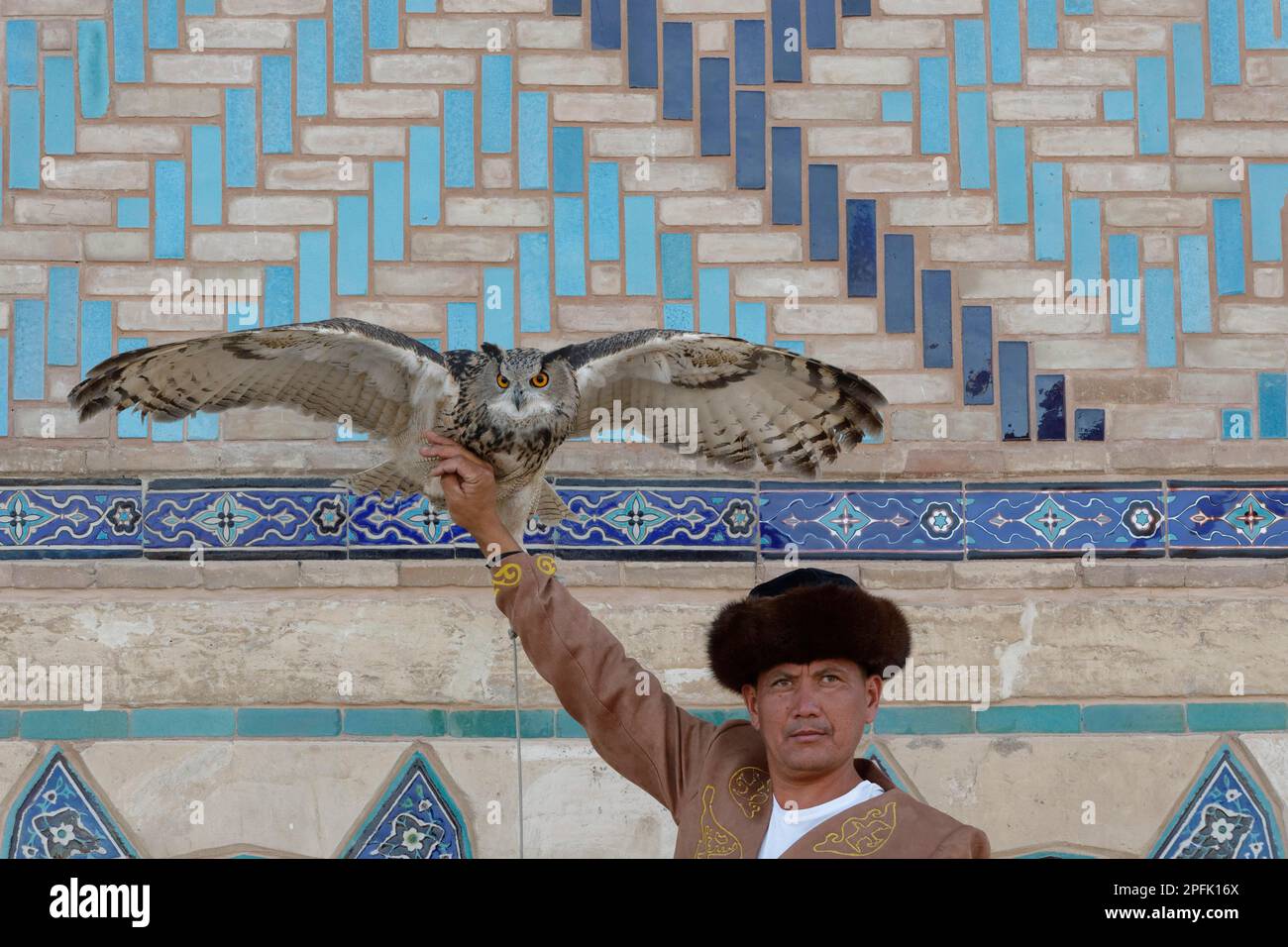 Kasachischer Mann in traditioneller Kleidung, der seine eurasische Adlereule (Bubo Bubo), Turkistan, Südregion, Kasachstan zeigt Stockfoto