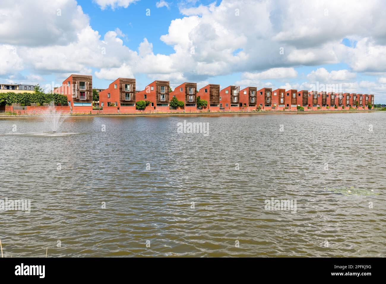 Eine Reihe moderner Häuser in einer Wohnanlage neben einem Teich an einem teilweise bewölkten Sommertag Stockfoto