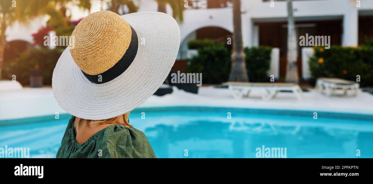 Eine nicht wiedererkennbare Frau mit Hut, die sich am Pool in einem luxuriösen Hotelresort erholt und einen perfekten Urlaub genießt. Banner mit Kopierbereich Stockfoto