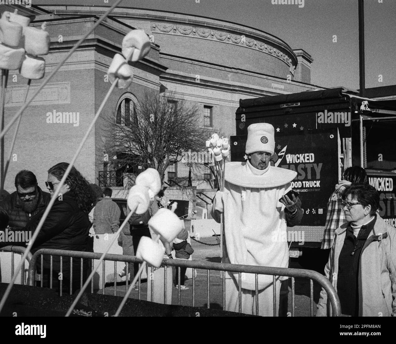 Ein Mann, der als Marshmallow verkleidet ist, hält eine Faust voller Spieße voller Marshmallows, die zum Rösten im Food Truck Court während des Winter Fest i bestimmt sind Stockfoto