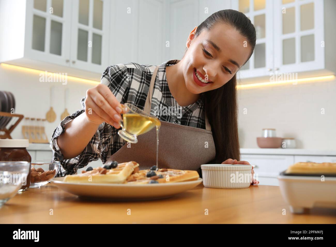Frau, die Honig auf leckere belgische Waffeln am Holztisch in der Küche schüttete Stockfoto