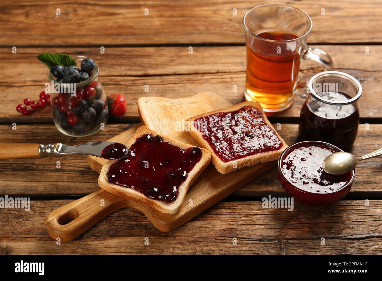 Köstliche Toasts mit verschiedenen Marmeladen, Tee und Beeren auf einem Holztisch Stockfoto