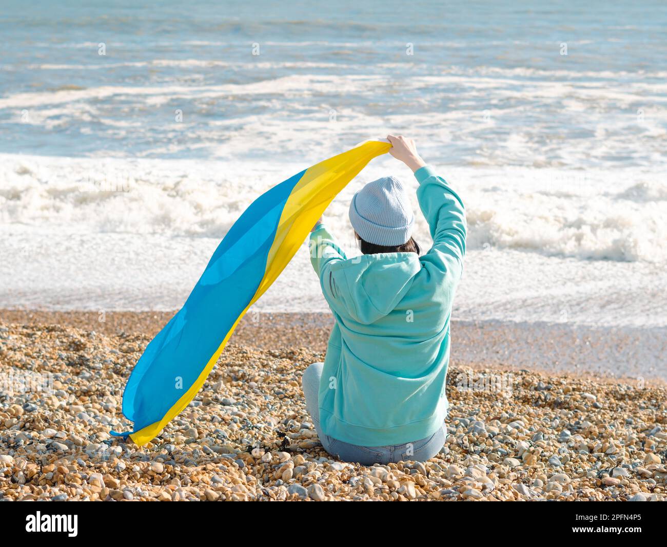 Braune Frau in blauem Hoodie und blauem Hut mit ukrainischer Nationalflagge, patriotisches Konzept Stockfoto