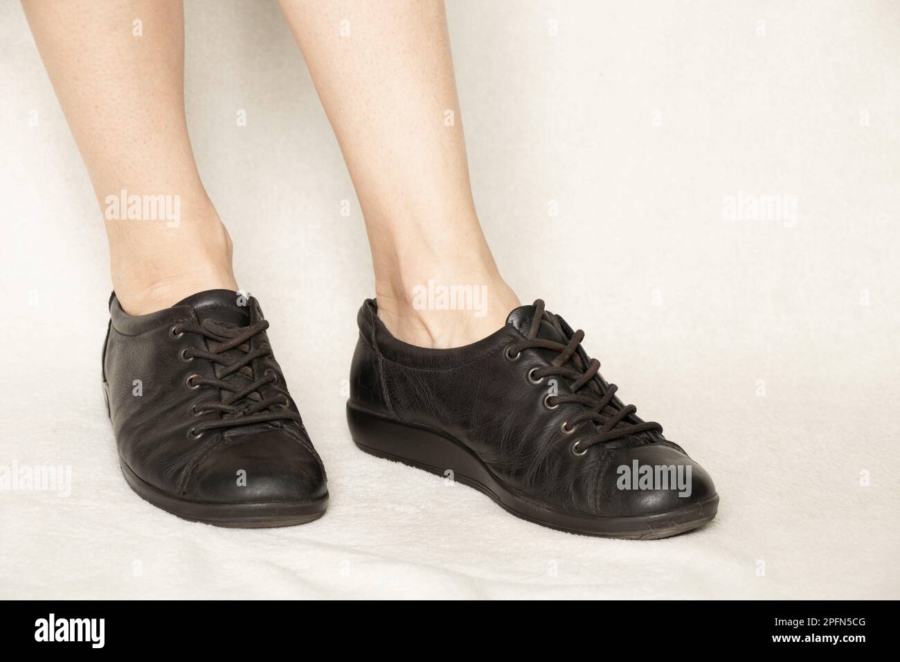 Schwarze Turnschuhe auf den Füßen eines Mädchens auf weißem Teppich, Schuhen und Mode Stockfoto