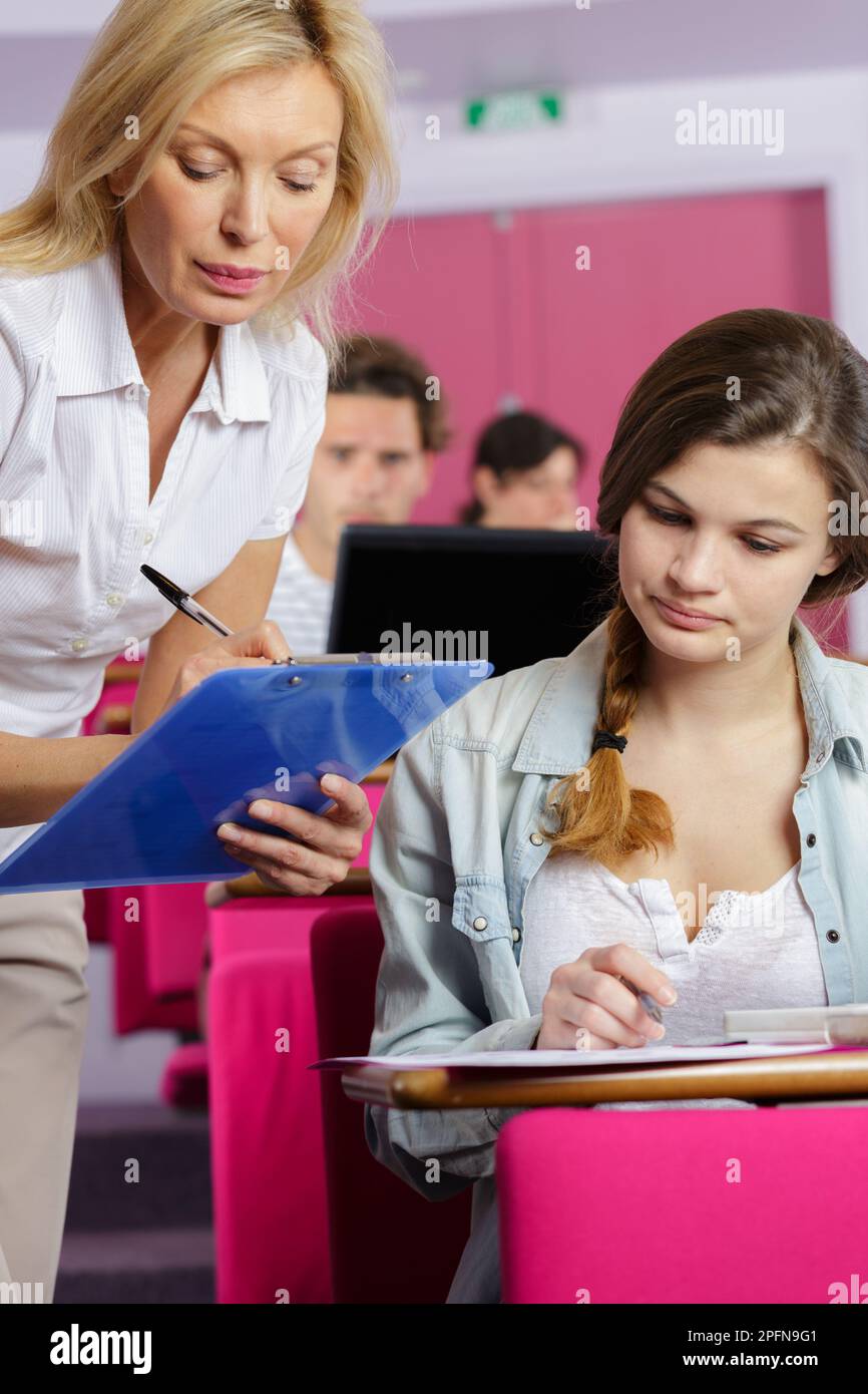 Der Lehrer stand neben dem Studenten und machte Notizen auf dem Klemmbrett Stockfoto