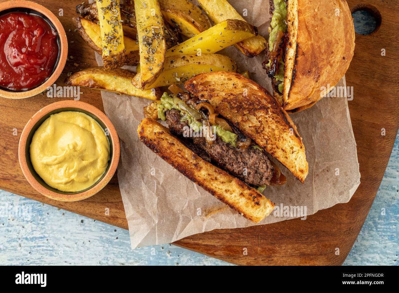 Karamellisierter Zwiebelburger mit Avocadosauce in zwei Hälften geschnitten, mit Saucen und pommes frites Stockfoto