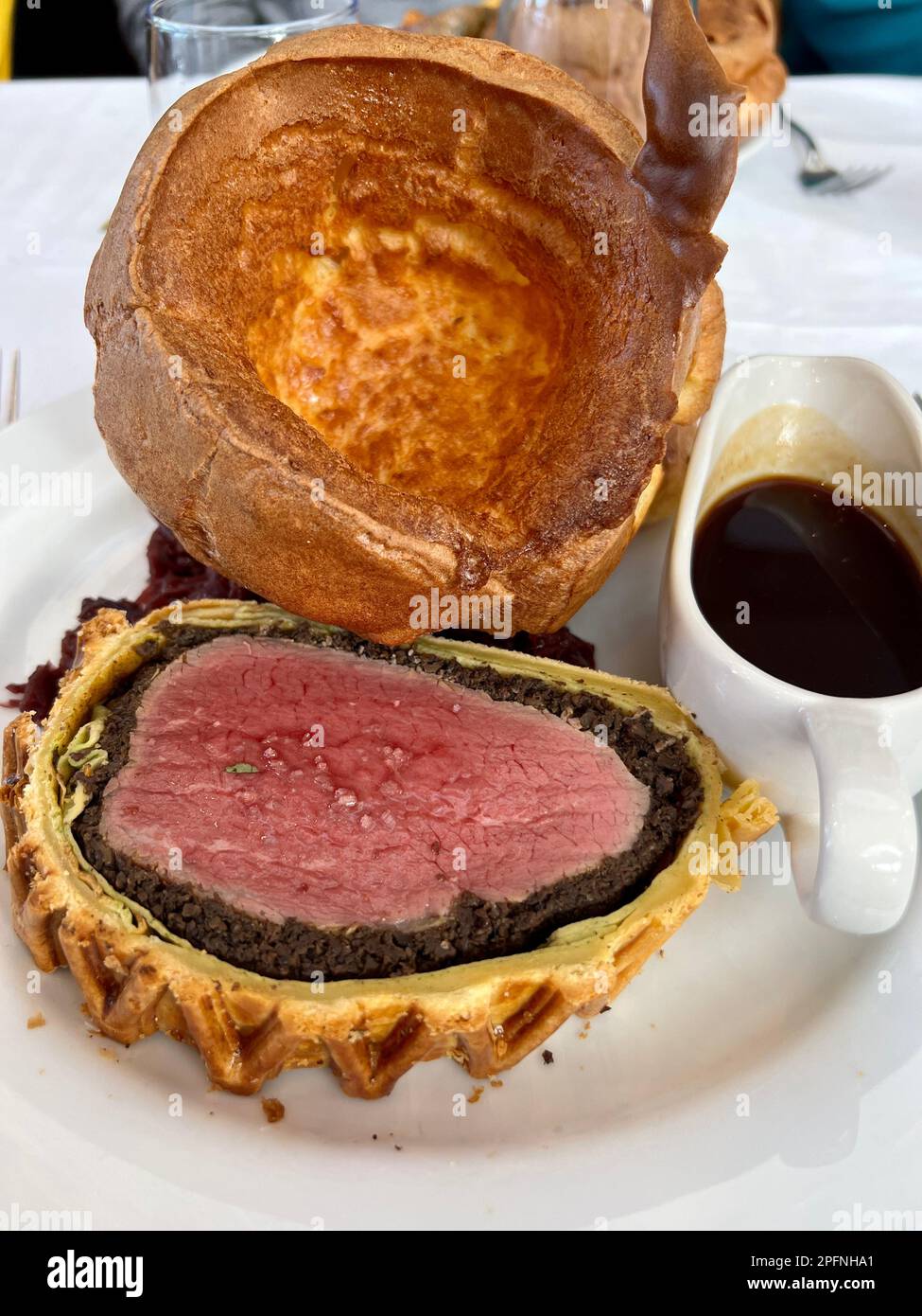 Gekochtes Rind Wellington mit Yorkshire Pudding und einer Beilage Soße auf einem weißen Teller und in einem Restaurant eingenommen. Stockfoto