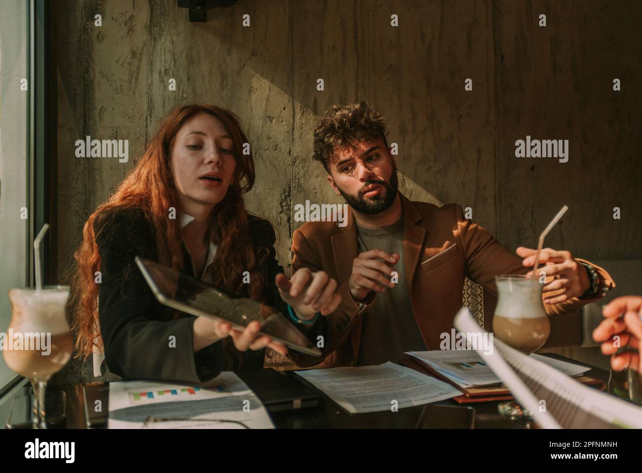 Attraktiver männlicher Geschäftsmann, der auf ein Tablet schaut. Seine rothaarige Kollegin zeigt ihm etwas Stockfoto