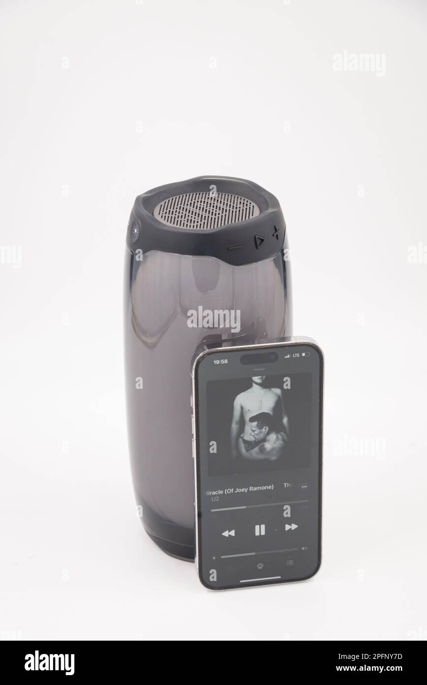 Riga, Lettland - 15. März 2023: Beispiel für eine Musik-Player-App auf einem Mobiltelefon vor einem kabellosen Lautsprecher auf weißem Hintergrund Stockfoto