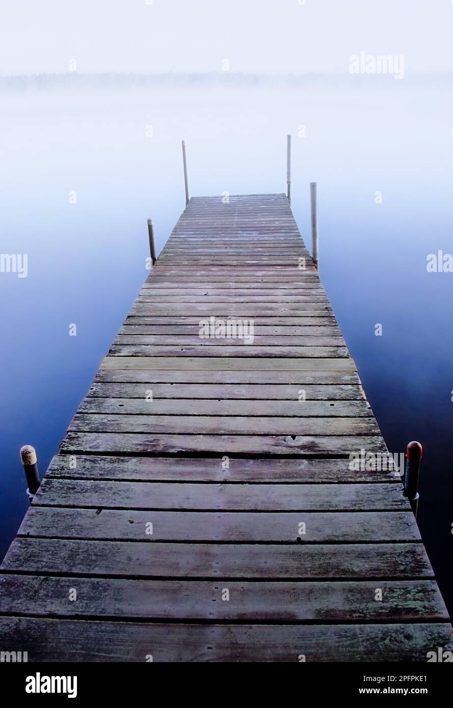 Ein Dock an einem See erstreckt sich früh am Morgen in die neblige Atmosphäre. Stockfoto