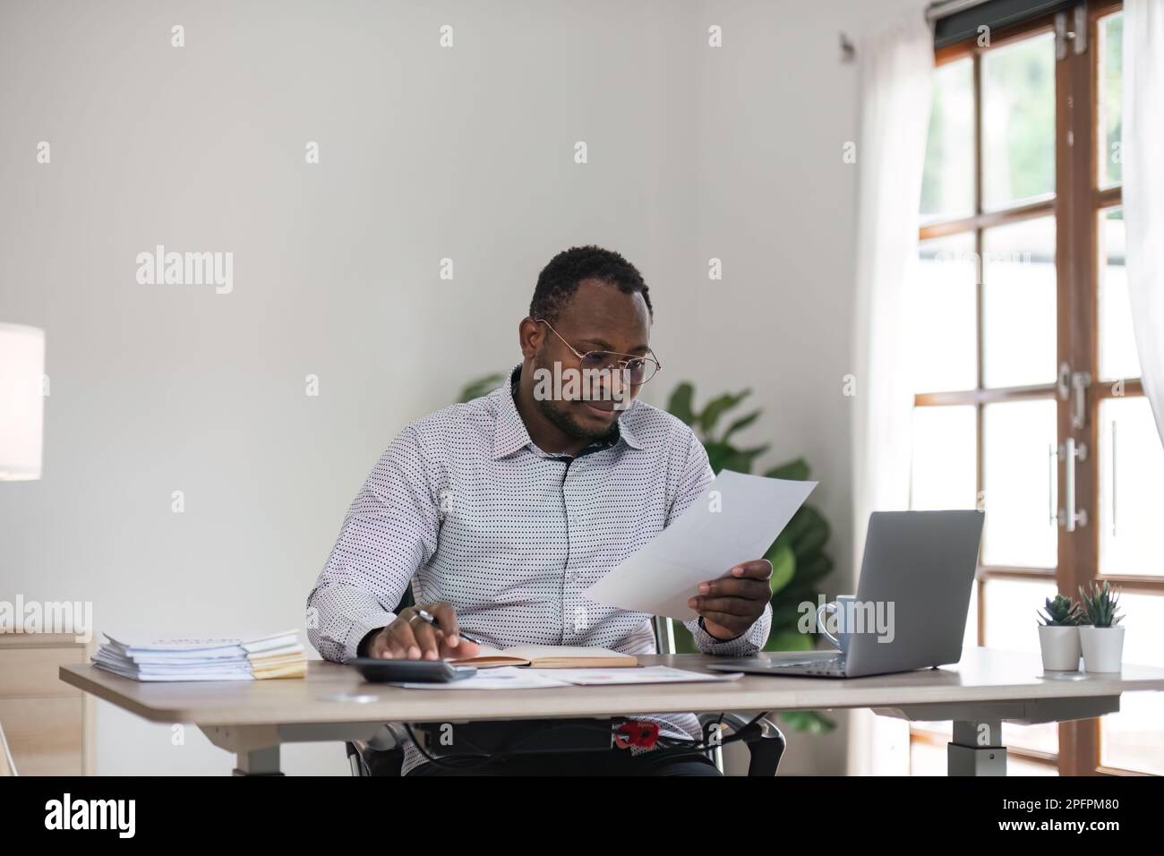 Fokussierter afrikanischer Geschäftsmann mit Dokumenten, der sich ein Notebook ansieht und recherchiert. Business Financial Analyst Konzept Stockfoto