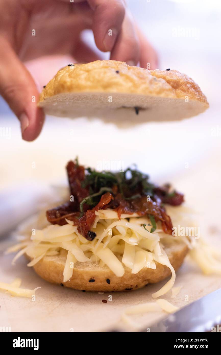 Der Koch bereitet einen Bagel mit Käse, Speck und Basilikum zu. Die Hand hält Brot Stockfoto