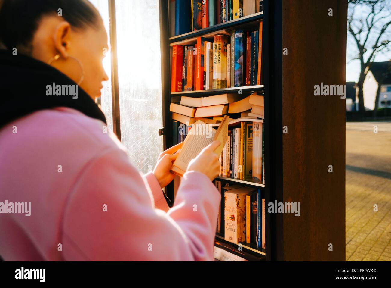 Junge weiße Frau, die Bücher in der kostenlosen öffentlichen Bibliothek im Stadtpark aussucht, um Bücher unter Lesern zu teilen. Stockfoto