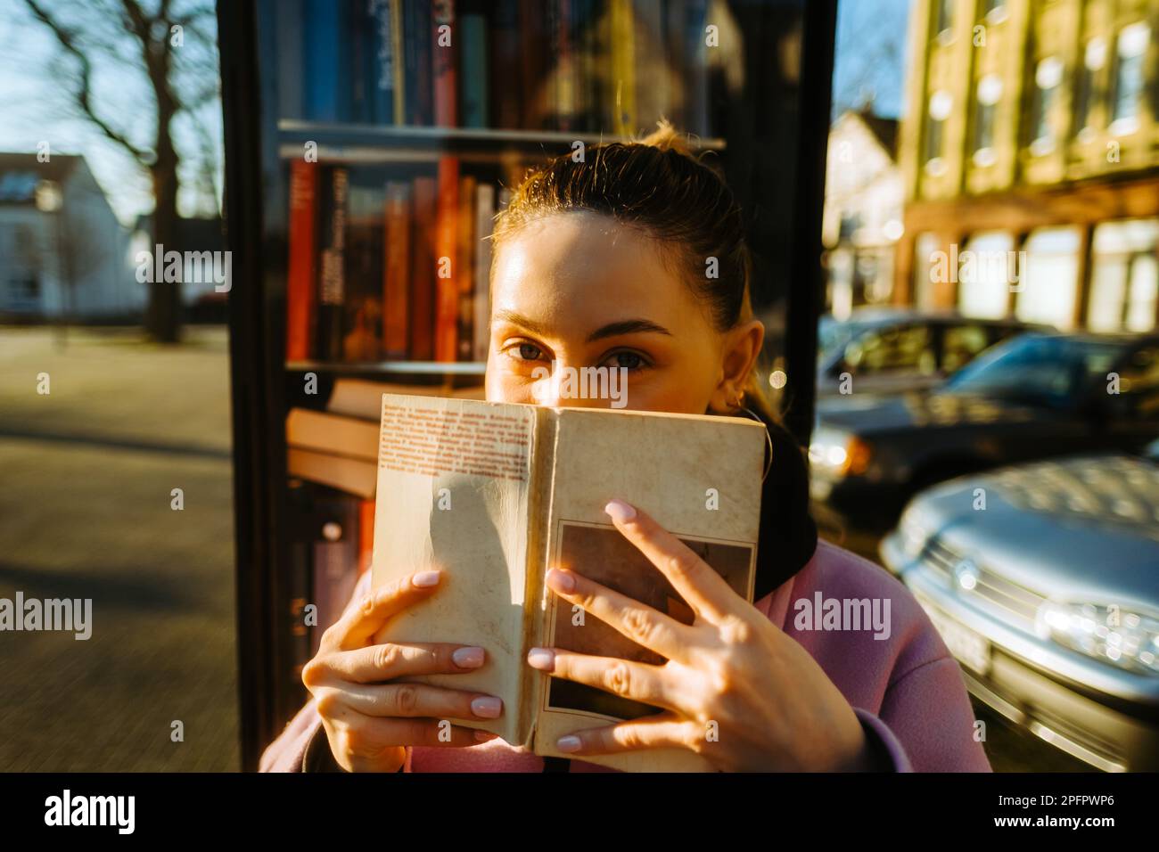 Porträt einer jungen, weiß-weißen Studentin, die sich hinter einem Buch versteckt und in die Kamera schaut. Stockfoto