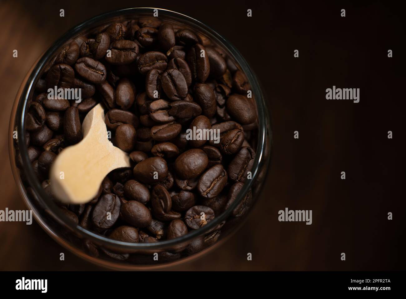 Kaffeebohnen werden auf dunklem Hintergrund in dunklem Holzboden mit Holzlöffel im Glasbecher angezeigt Stockfoto