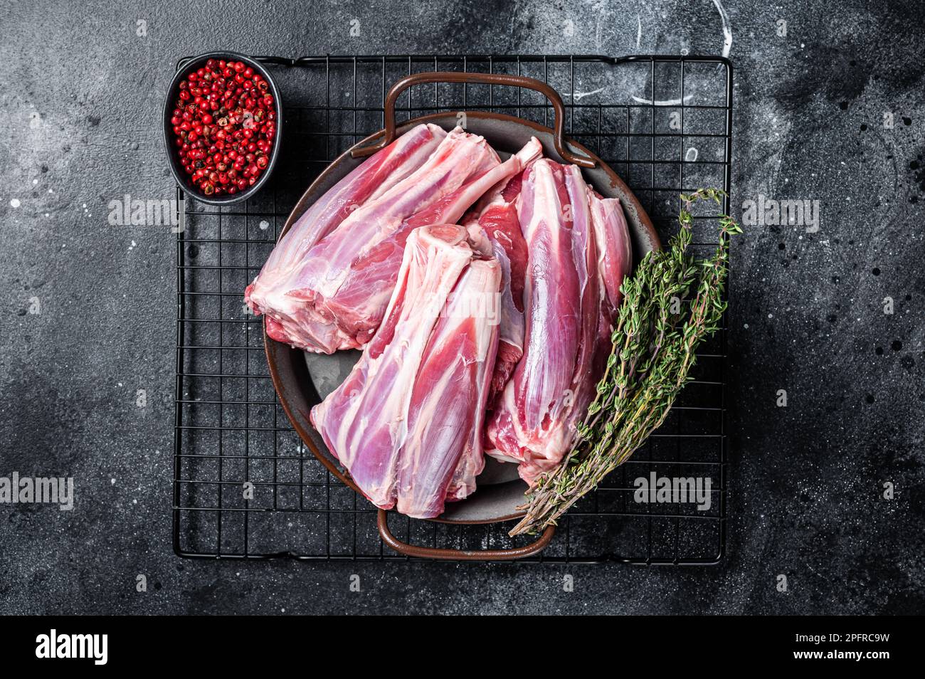 Rohe Lammschenkelschäfte in einer Stahlschale mit Kräutern. Schwarzer Hintergrund. Draufsicht. Stockfoto