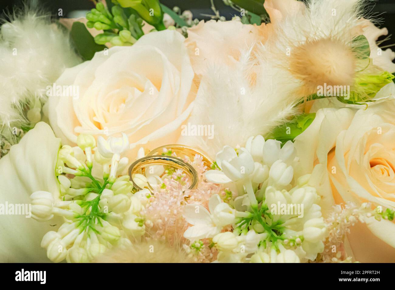 Goldene Eheringe liegen in grünem, weißem Hochzeitsstrauß mit frischen Blumen Stockfoto