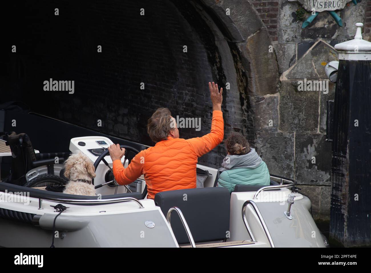 04 23. Oktober 2021, Leiden, Niederlande, Rückansicht eines glücklichen erwachsenen Ehepaars und Hundes auf dem Boot, Grüße an Freunde während der Fahrt auf den Kanälen o Stockfoto