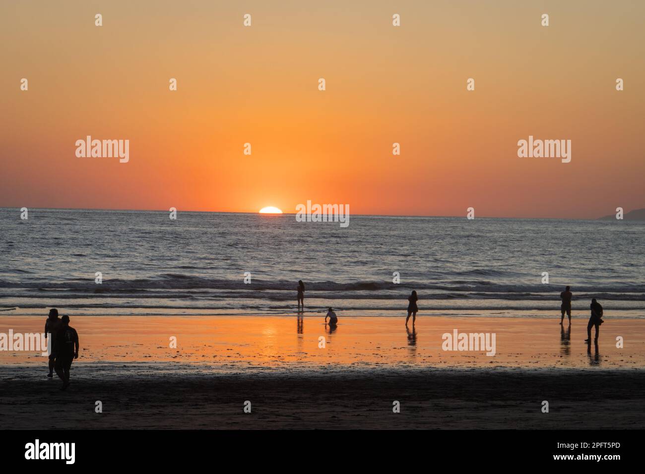 Die untergehende Sonne verschwindet unter dem Horizont am Strand, während die Menschen das Licht in Jaco, Costa Rica, genießen Stockfoto