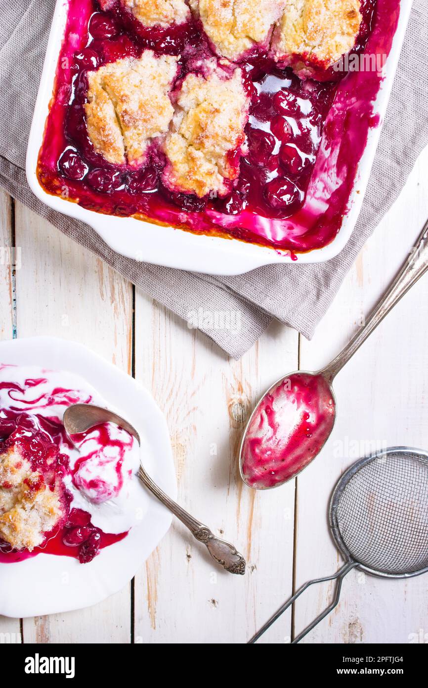 Hausgemachte Kirschkuchen mit knuspriger Kruste, Eis, altem Löffel, Sieb für Mehl. Draufsicht auf dem weißen Holztisch Stockfoto