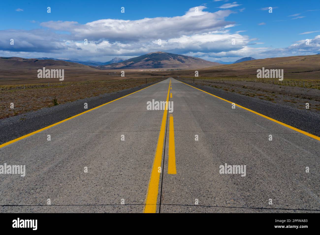 Eine lange, gerade Straße mit gelben Linien, die in Richtung Berge führt, die die Atacama-Wüste in Chile kreuzen. Sonne mit Wolken am blauen Himmel. Stockfoto