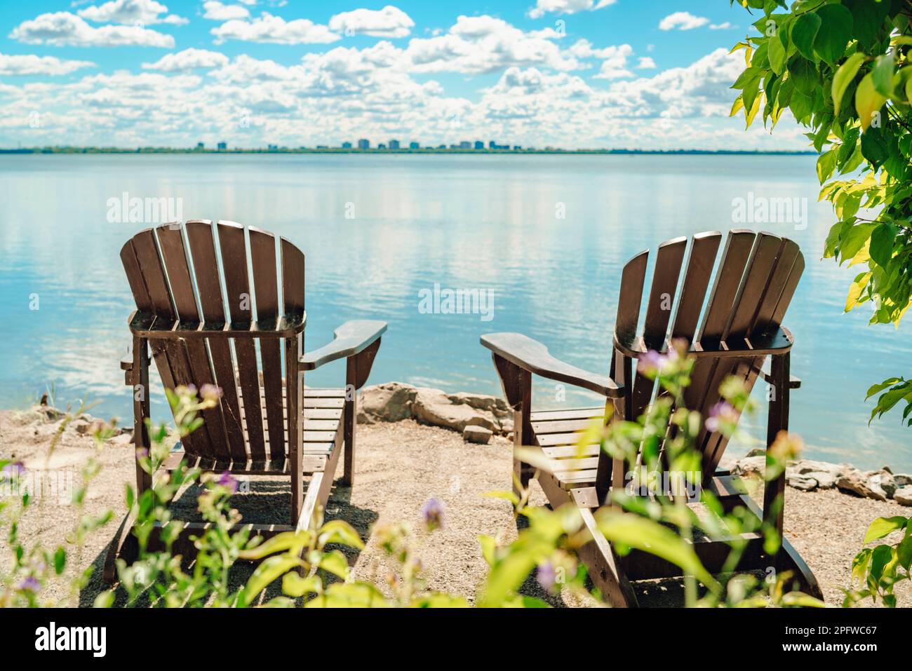 Zwei Muskoka-Stühle am Wasser auf der Terrasse mit ruhigem Blick auf den kanadischen See. Sommer Cottage Urlaub Lifestyle Stockfoto