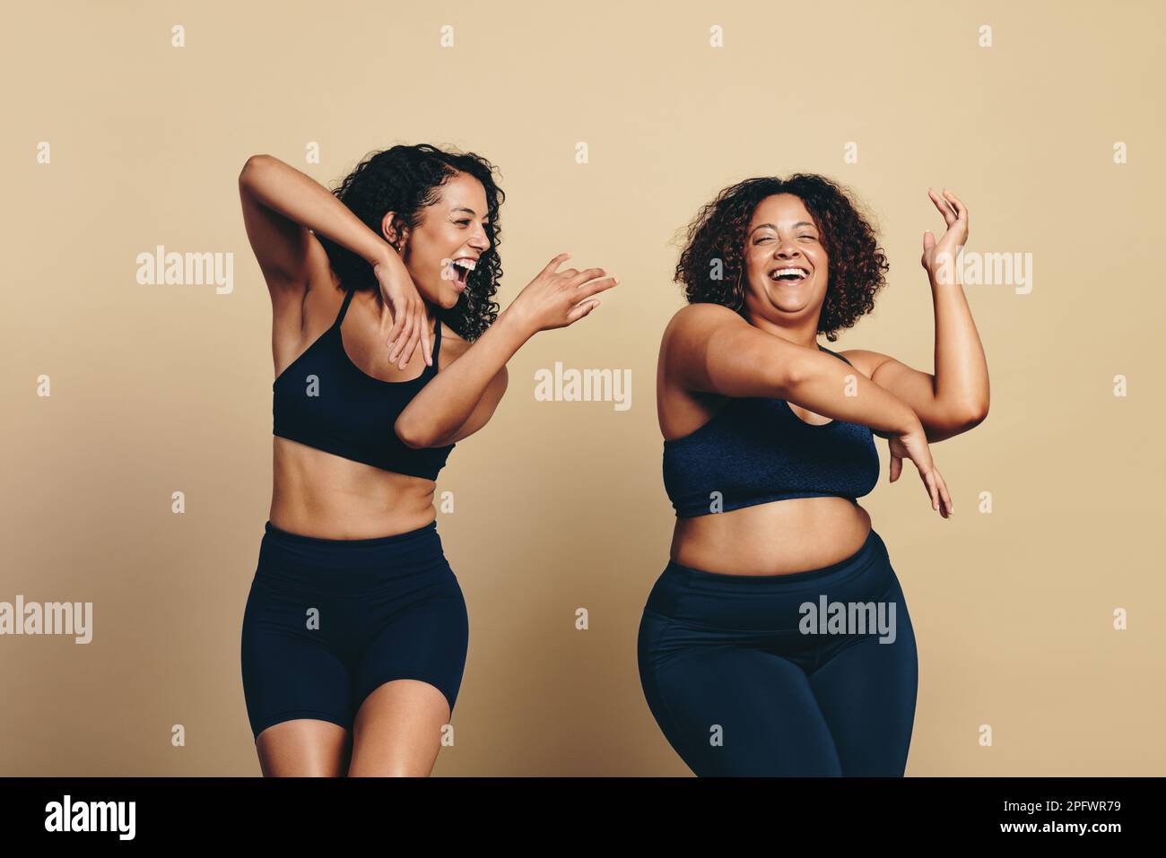 Zwei junge Frauen, die Sportkleidung tragen und voller Vitalität tanzen und trainieren, zusammen in einem Studio. Glückliche Sportlerinnen, die Spaß haben und feiern Stockfoto