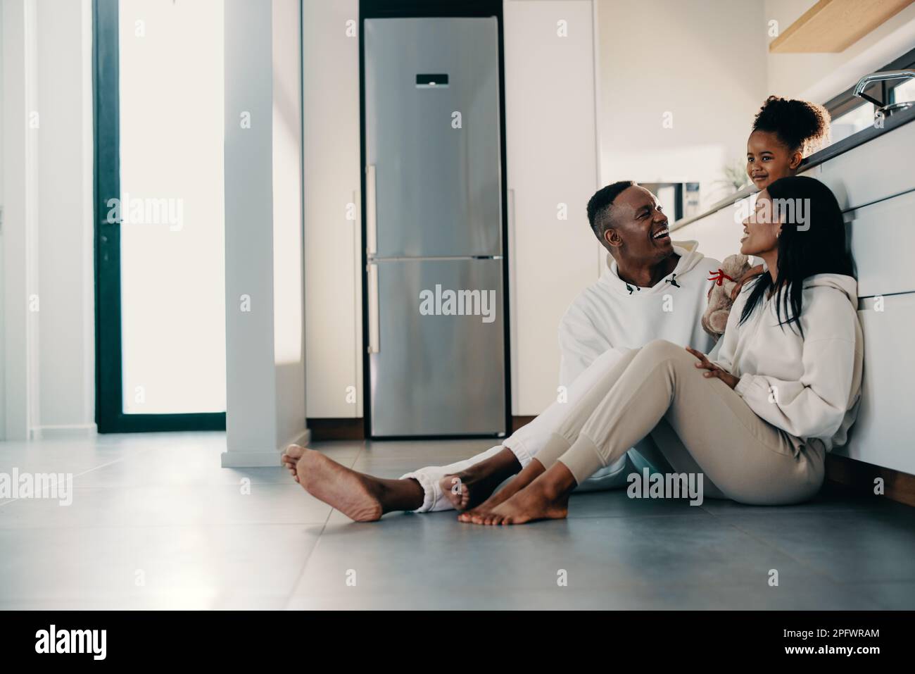 Mom und Dad sitzen auf dem Küchenboden mit ihrer Tochter. Junge schwarze Eltern haben Familienmomente mit ihrem einzigen Kind zu Hause. Spaß für die Familie Stockfoto