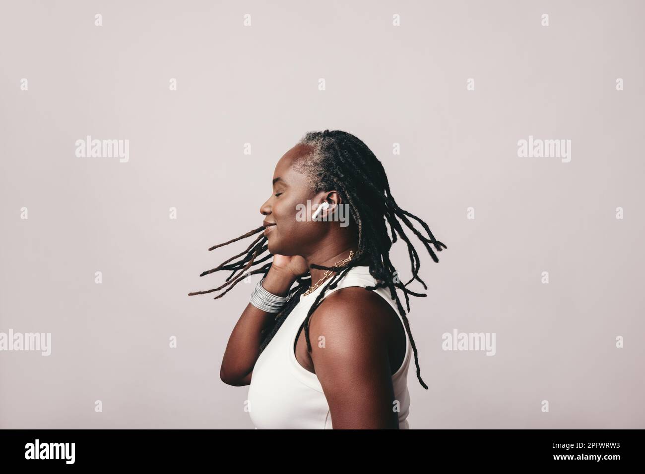 Frau mittleren Alters mit Dreadlocks, die ihre Lieblingsmusik über bluetooth-Ohrstöpsel genießt. Modische, reife Frau, die eine Playlist hört, während sie A steht Stockfoto