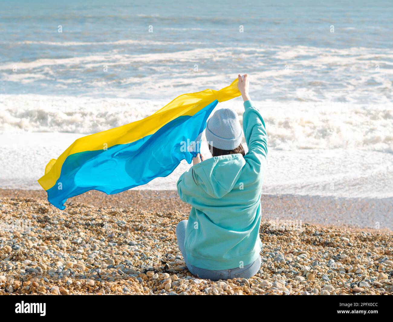 Braune Frau in blauem Hoodie und blauem Hut mit ukrainischer Nationalflagge, patriotisches Konzept Stockfoto