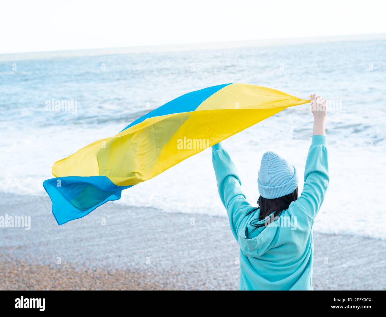 Braune Frau in blauem Hoodie und blauem Hut mit ukrainischer Nationalflagge, patriotisches Konzept Stockfoto