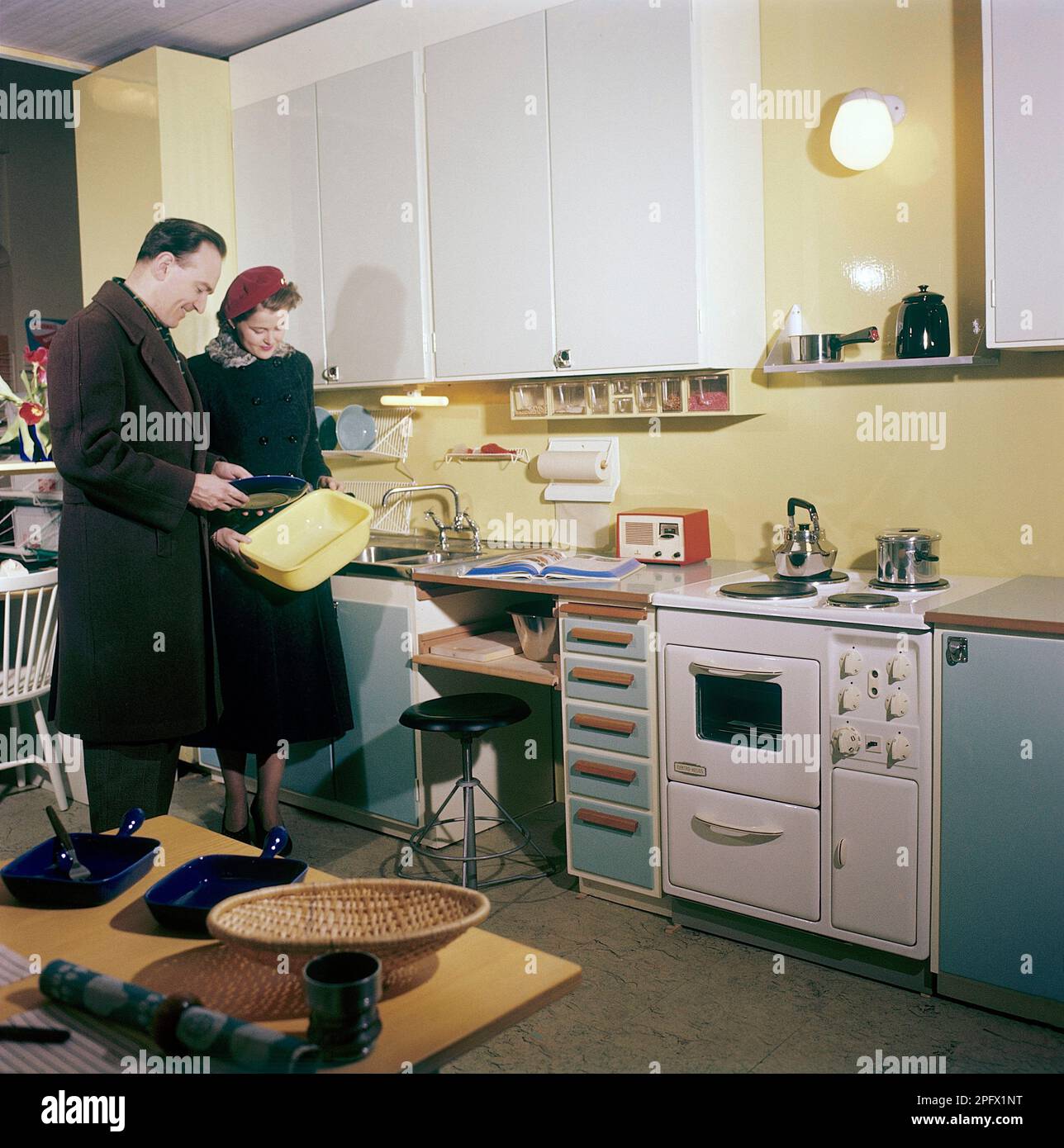 In der Küche 1950er. Ein junges Paar in einer Küche, entworfen und mit Gegenständen, Haushaltsgeräten und Details, die sehr typisch für das 1950er. Jahrzehnt sind. Alles in der Küche ist zu dieser Zeit brandneu und zeigt das Neueste an Design und Funktion. Schweden 1958. Conard Ref BV42-2 Stockfoto