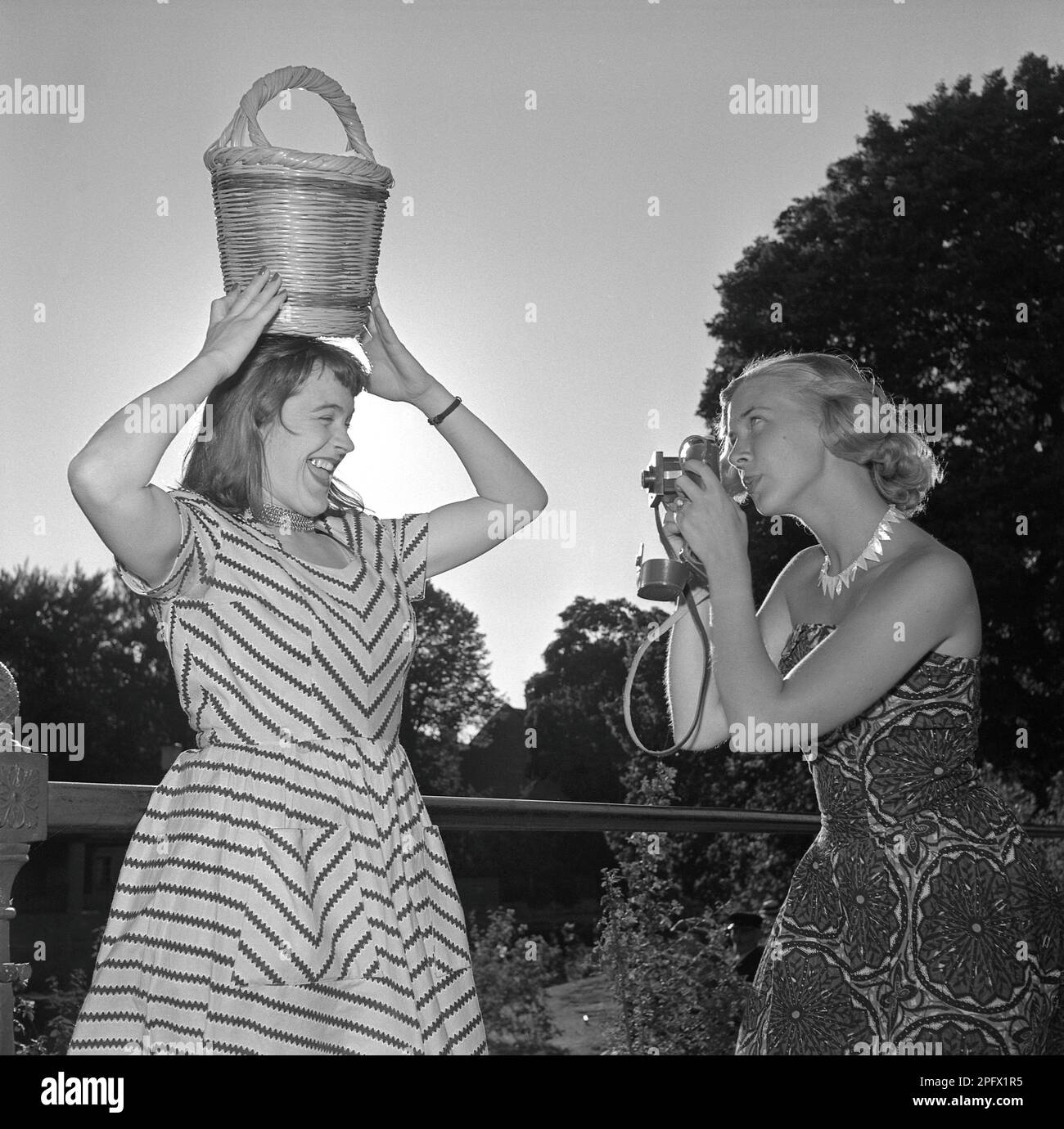 Fotograf in den 1950er. Eine junge Frau fotografiert an einem Sommertag. Eine Freundin von ihr posiert für sie und hält einen Korb über ihrem Kopf. Schweden 1951. Conard Ref. 1752 Stockfoto